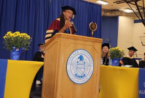 Marina Barnett addresses students from the podium in her academic regalia. 