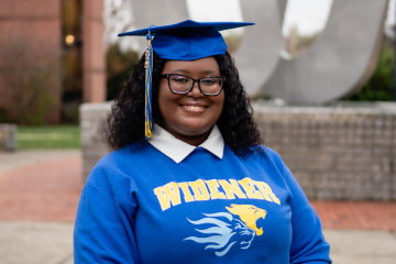Taylor Easter smiles at the camera wearing a blue graduation cap and blue Widener sweatshirt