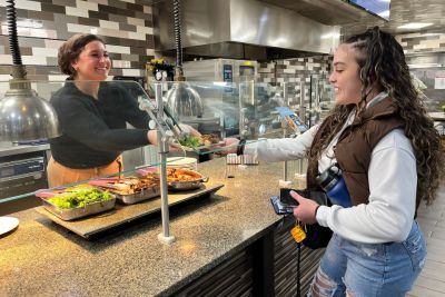 Dietitian Nora Abraham in the kitchen handing a plate of food to student Maritza Garcia ’25 