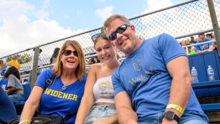Parents and their daughter pose in Widener T-shirts in the stands during the Homecoming football game on Widener's campus.