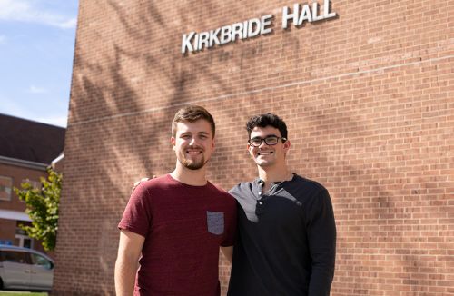 Sean Crook and Nick Lambert pose and smile outside of Kirkbride Hall
