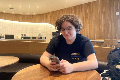 Student sitting in campus coffee shop looking at phone, using app