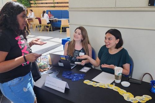 Employees seated at decorated table interacting with student standing across from them